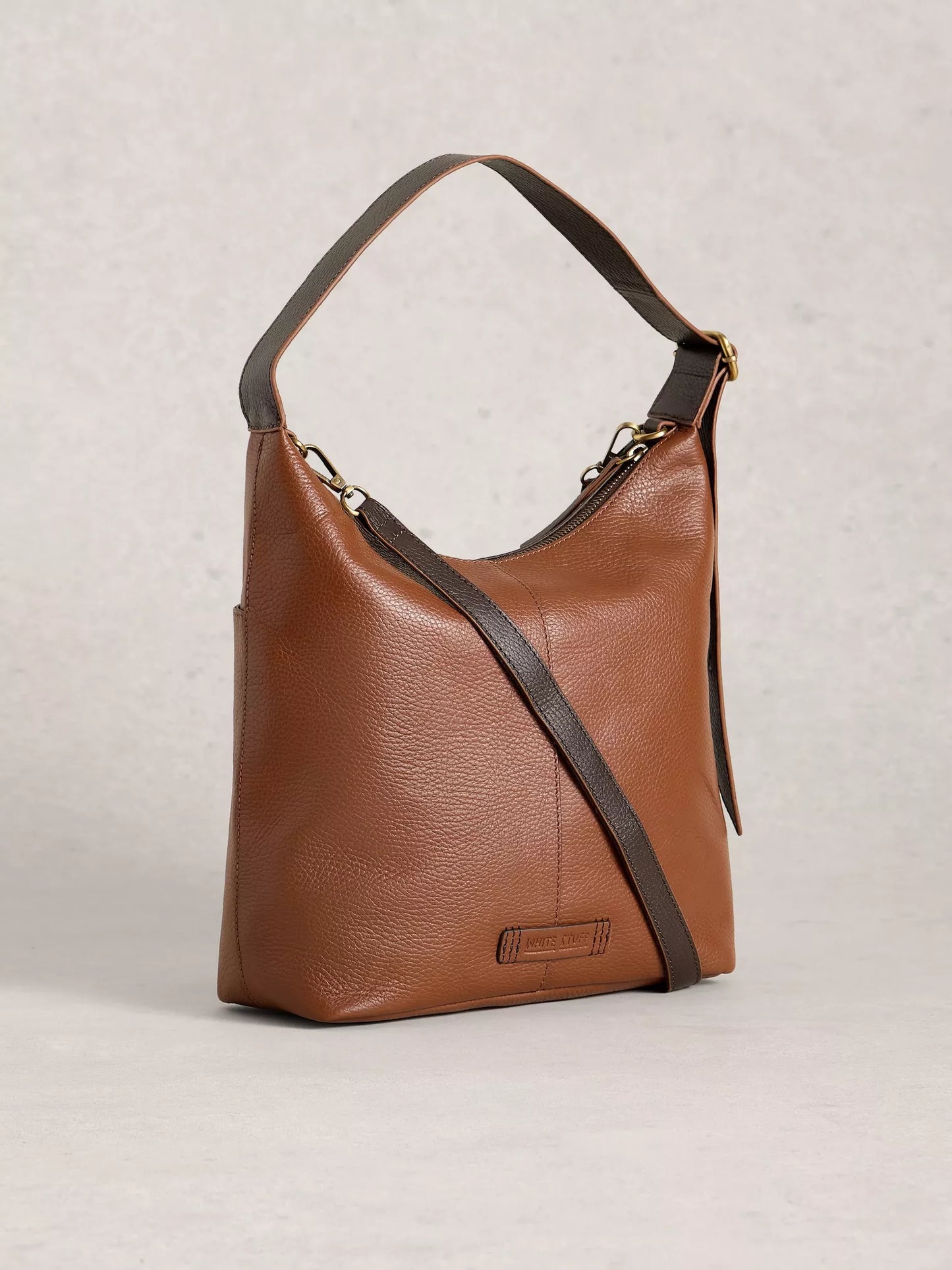 Brown leather handbag with a shoulder strap on a light gray background