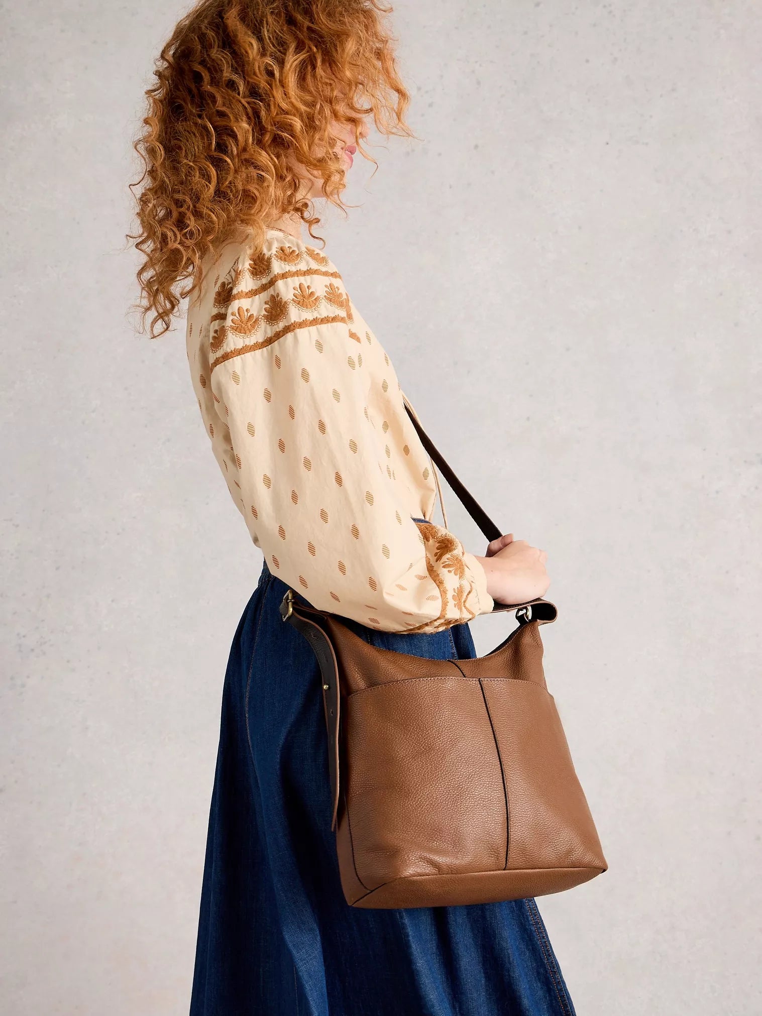 Woman holding a brown leather handbag against a plain background