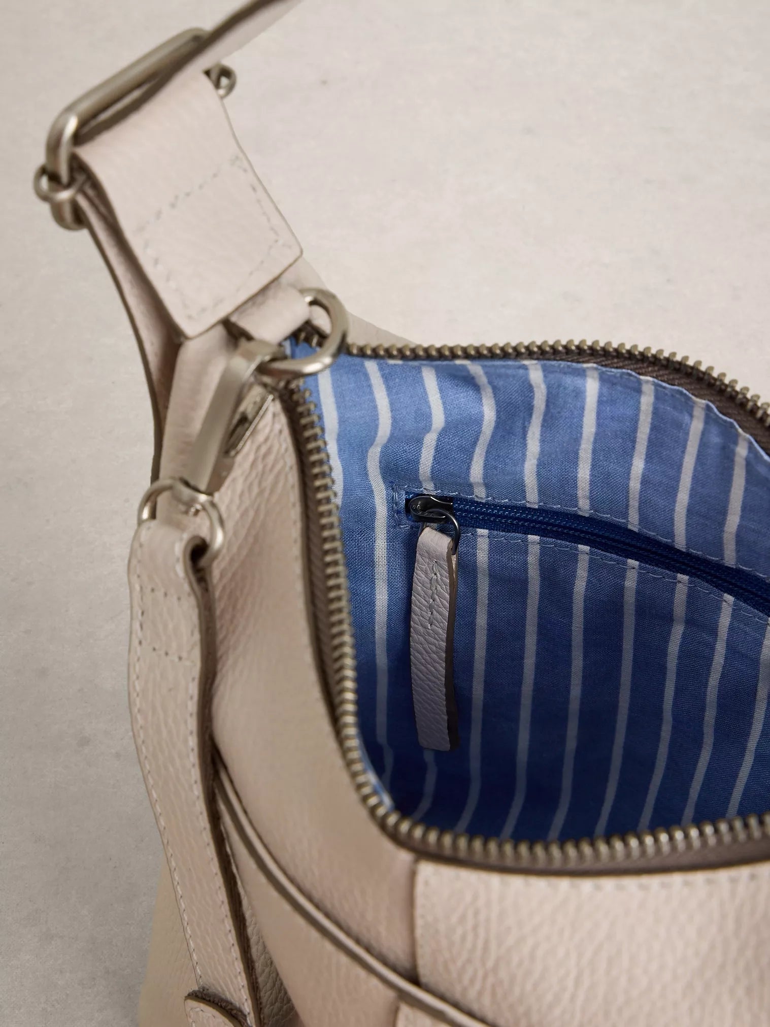 Close-up of a beige handbag with a blue striped interior pocket.