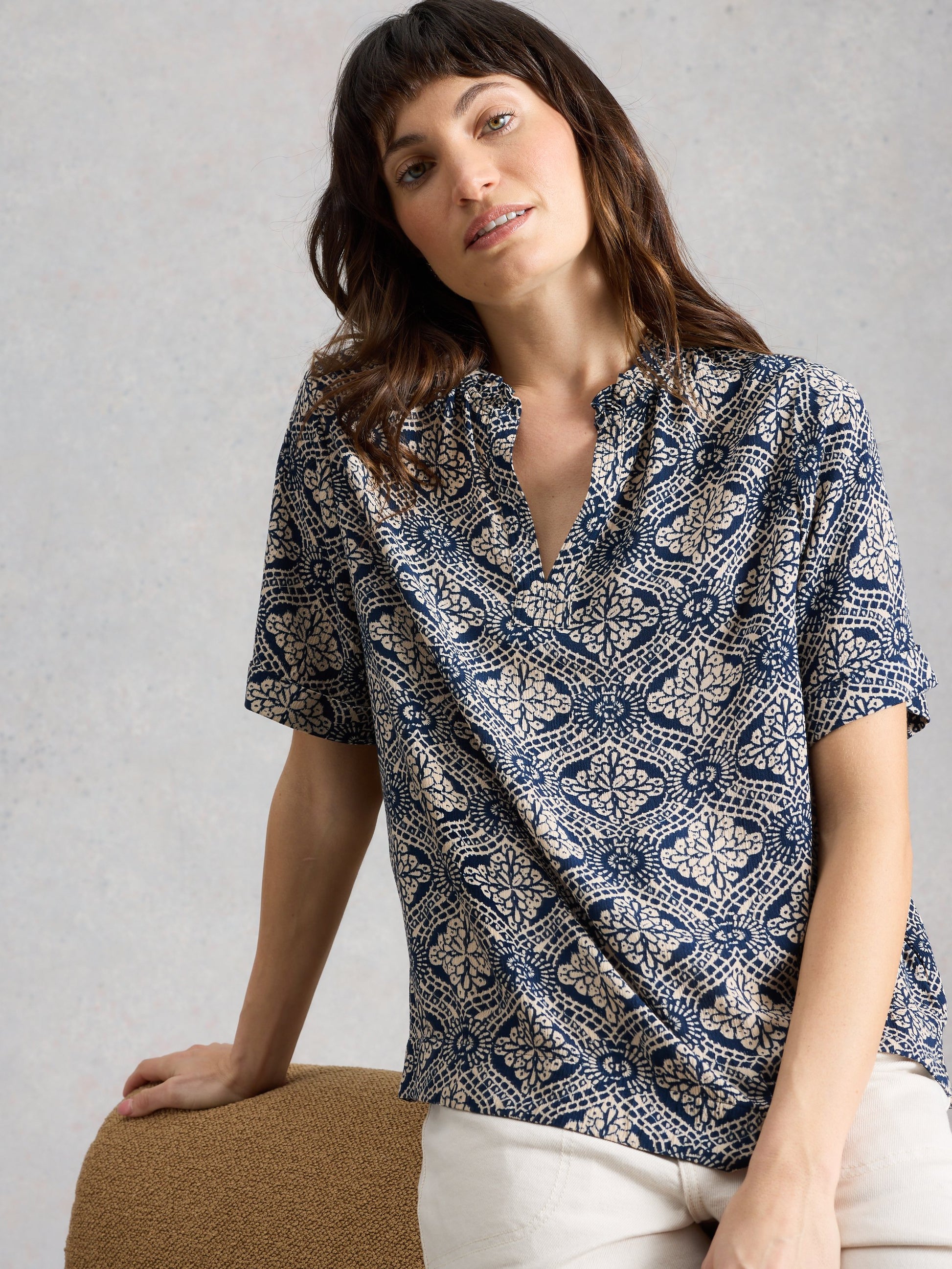 Woman wearing a patterned shirt sitting on a chair against a plain background