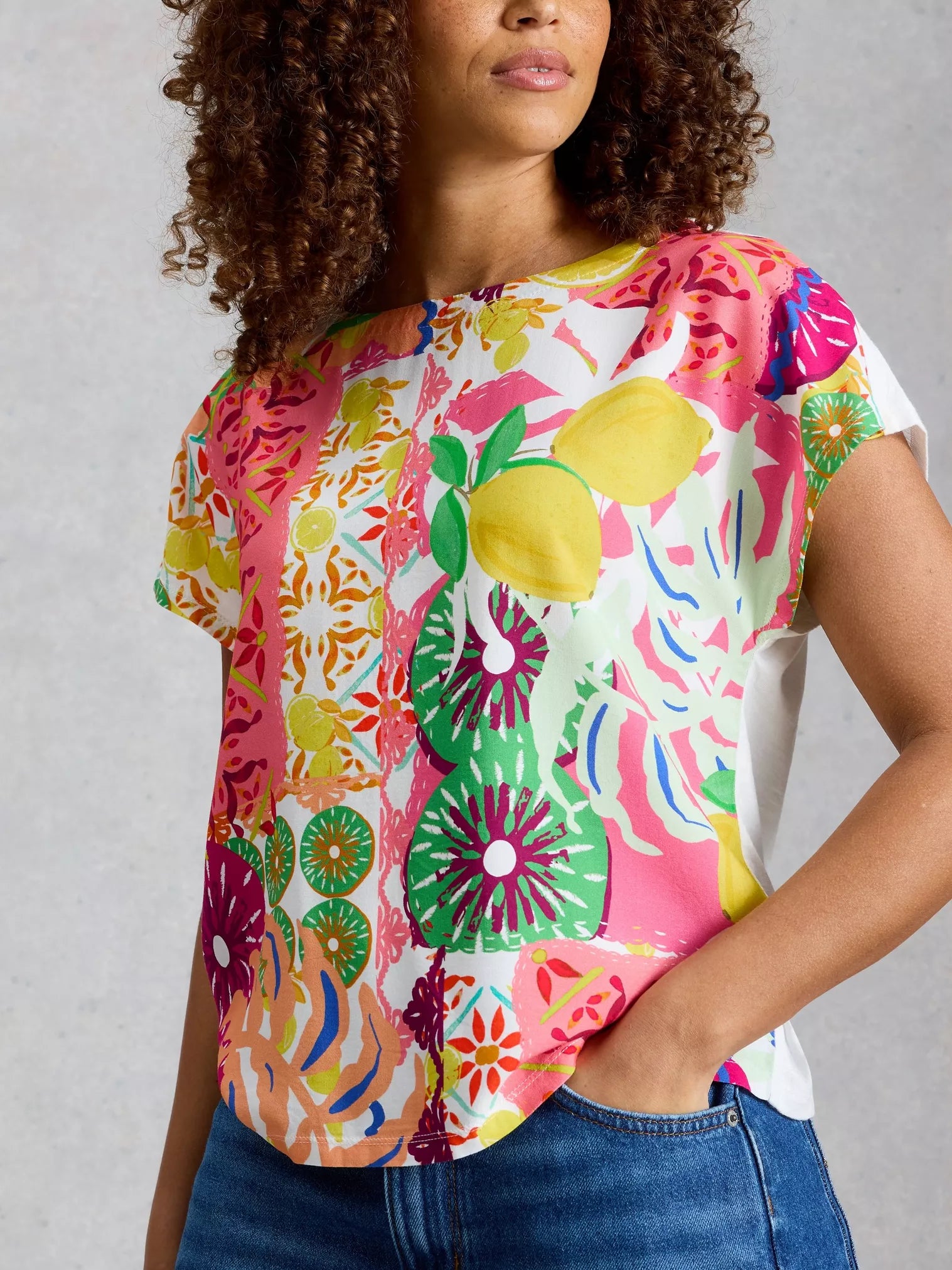 Woman wearing a colourful floral and fruit patterned shirt against a plain background