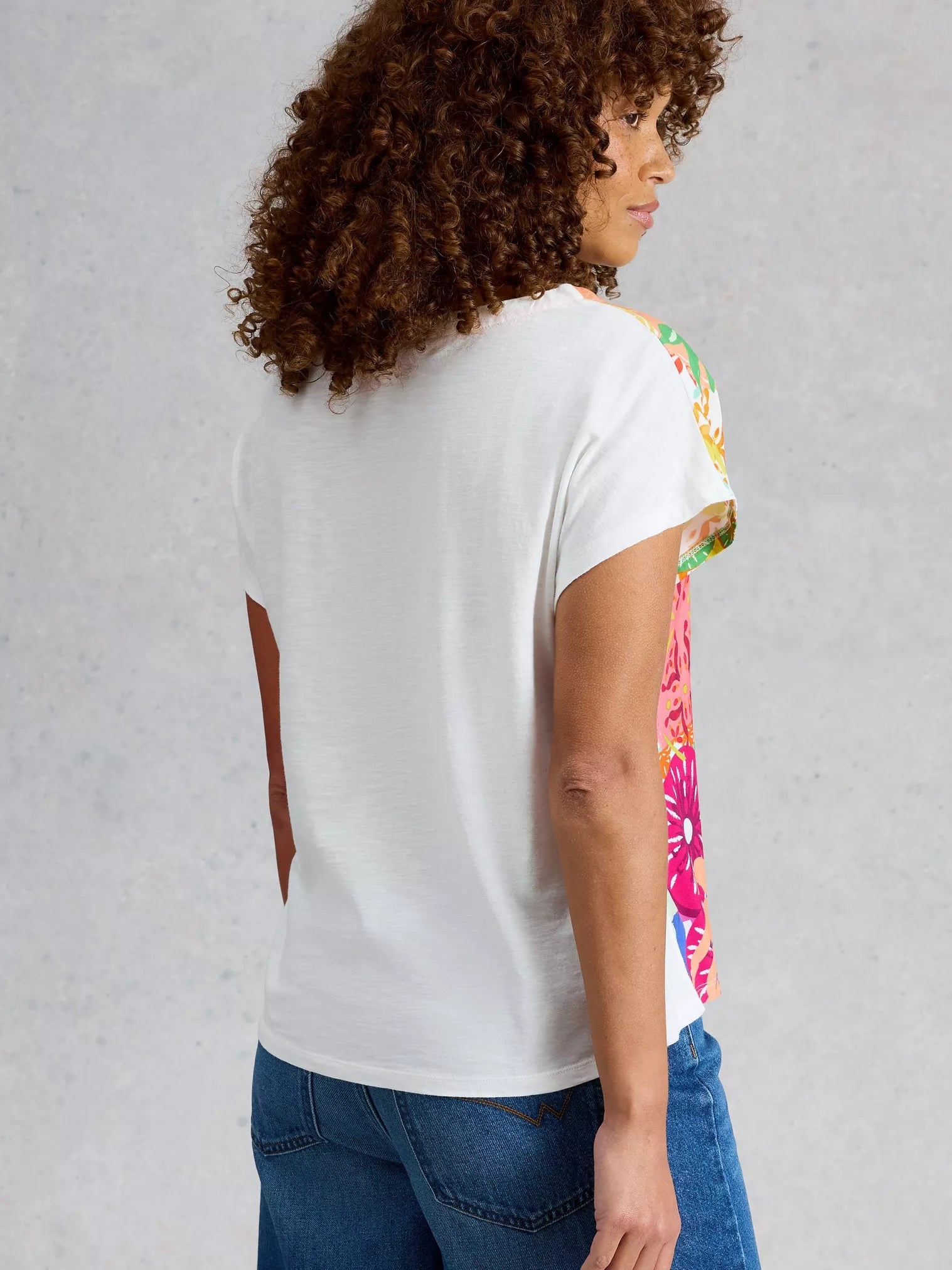 Person wearing a white t-shirt with colorful floral sleeves against a gray background