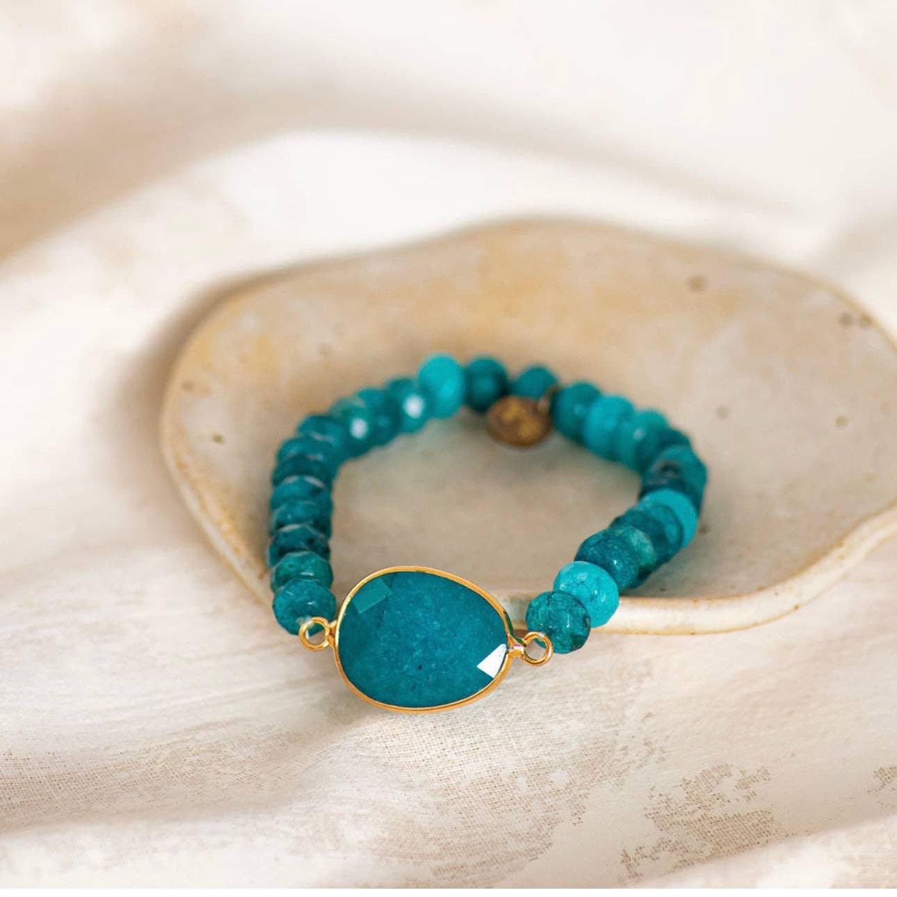 Turquoise beaded bracelet with a gold accent on a beige stone background