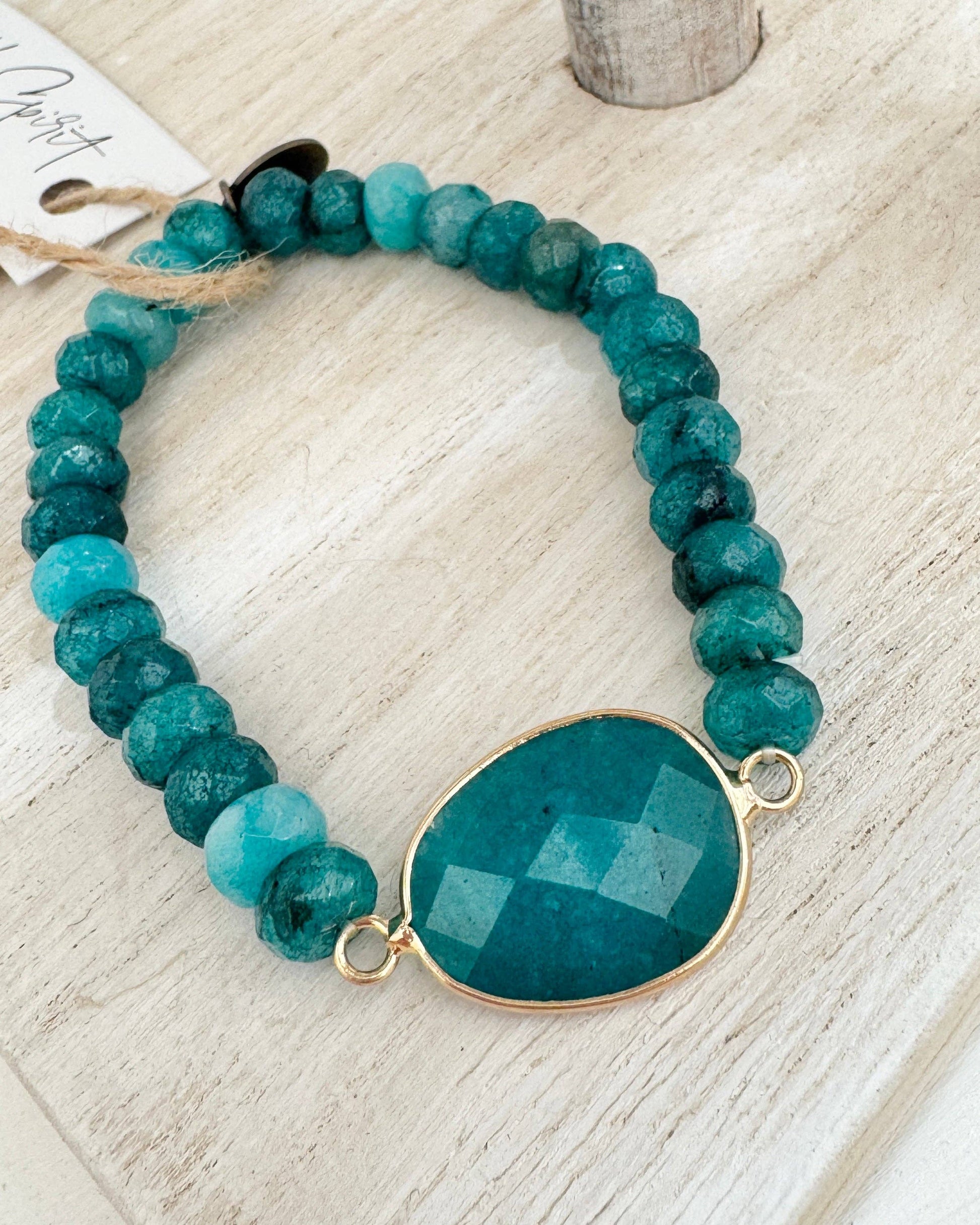 Teal beaded bracelet with a gold accent on a light wooden surface