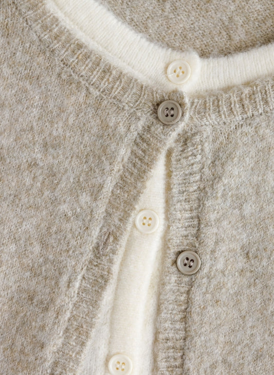 Close-up of a knit cardigan with a heathered light beige body and an off-white ribbed trim, featuring four buttons down the front.