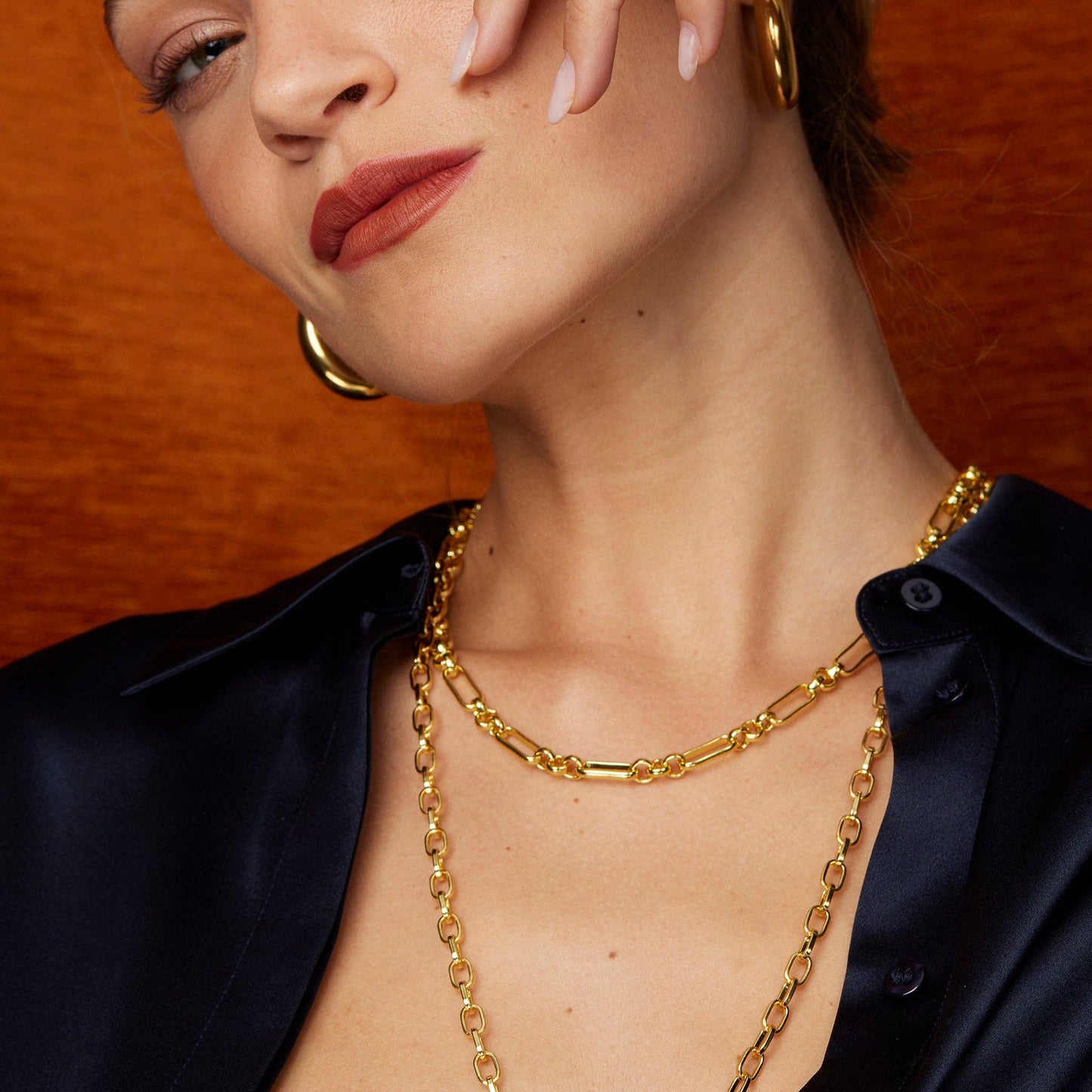 Woman wearing gold hoop earrings and a gold chain necklace against an orange background