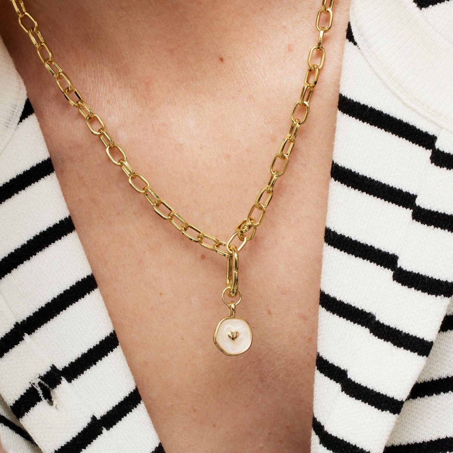 Gold chain necklace with a pendant on a person wearing a black and white striped garment.