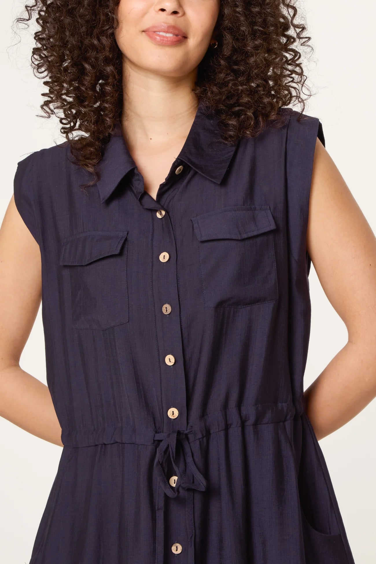 Navy sleeveless dress with button details on a plain background